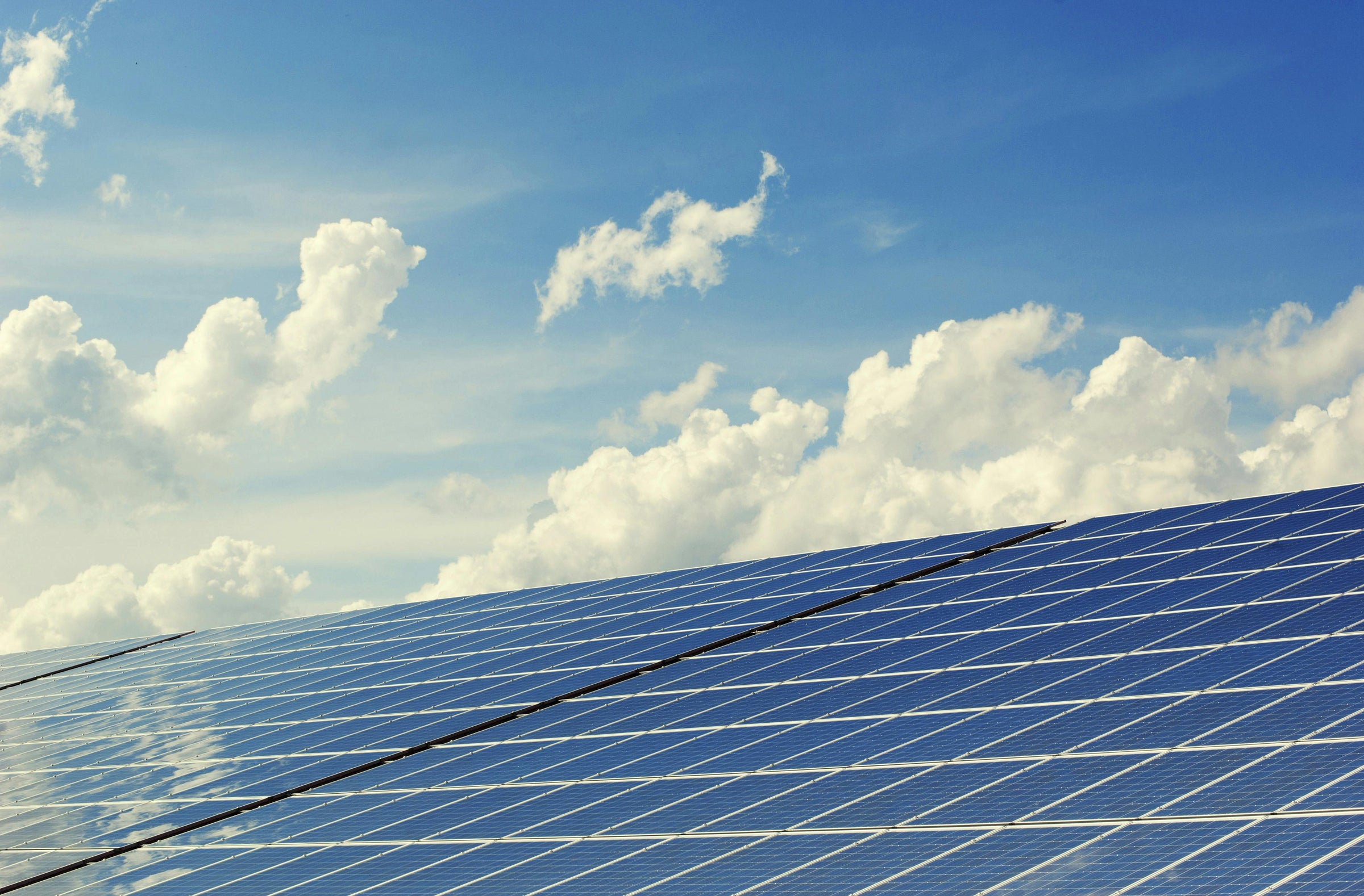 Solar panels reflecting sunlight against a bright blue sky with fluffy white clouds.