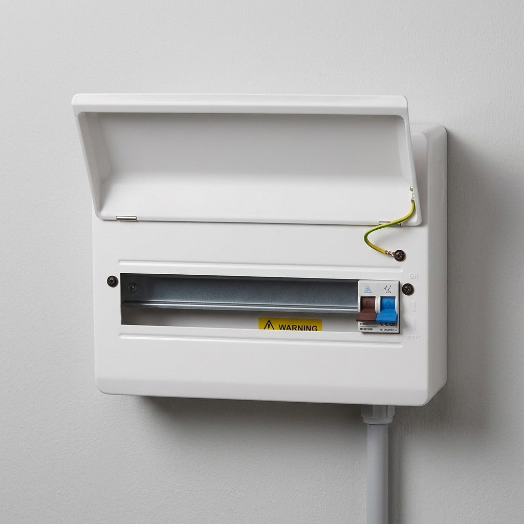 A white electrical distribution board or switchbox mounted on a light gray wall, with the lid open, showing a metal busbar, a yellow warning label, and a small blue-and-white switch.