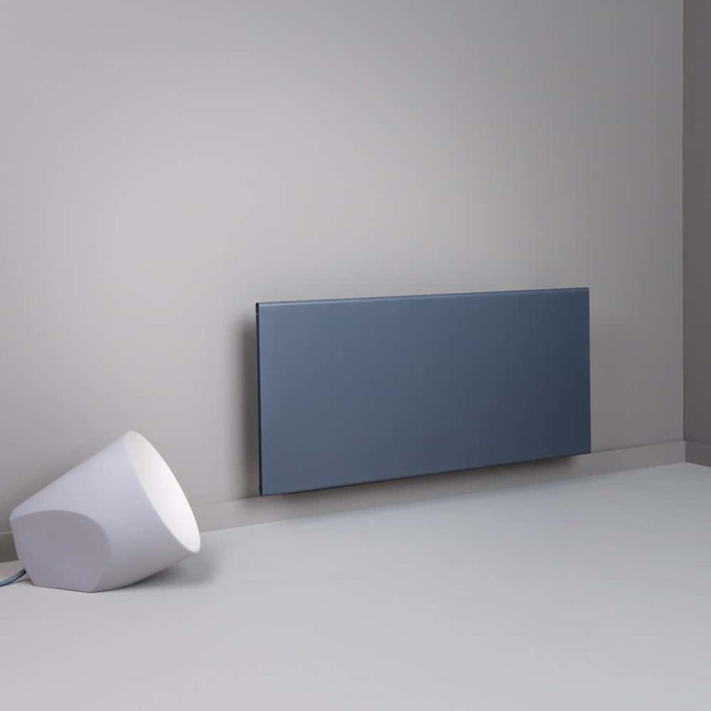 Modern electric panel heater against a plain wall with a white lamp on the floor.