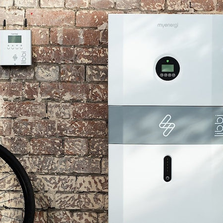 Energy storage system branded 'myenergi' against a brick wall with a bicycle partially visible.