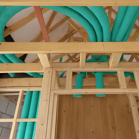 Green semi-rigid duct insulation pipes installed inside a wooden frame structure, showing the installation details on a roof or wall.