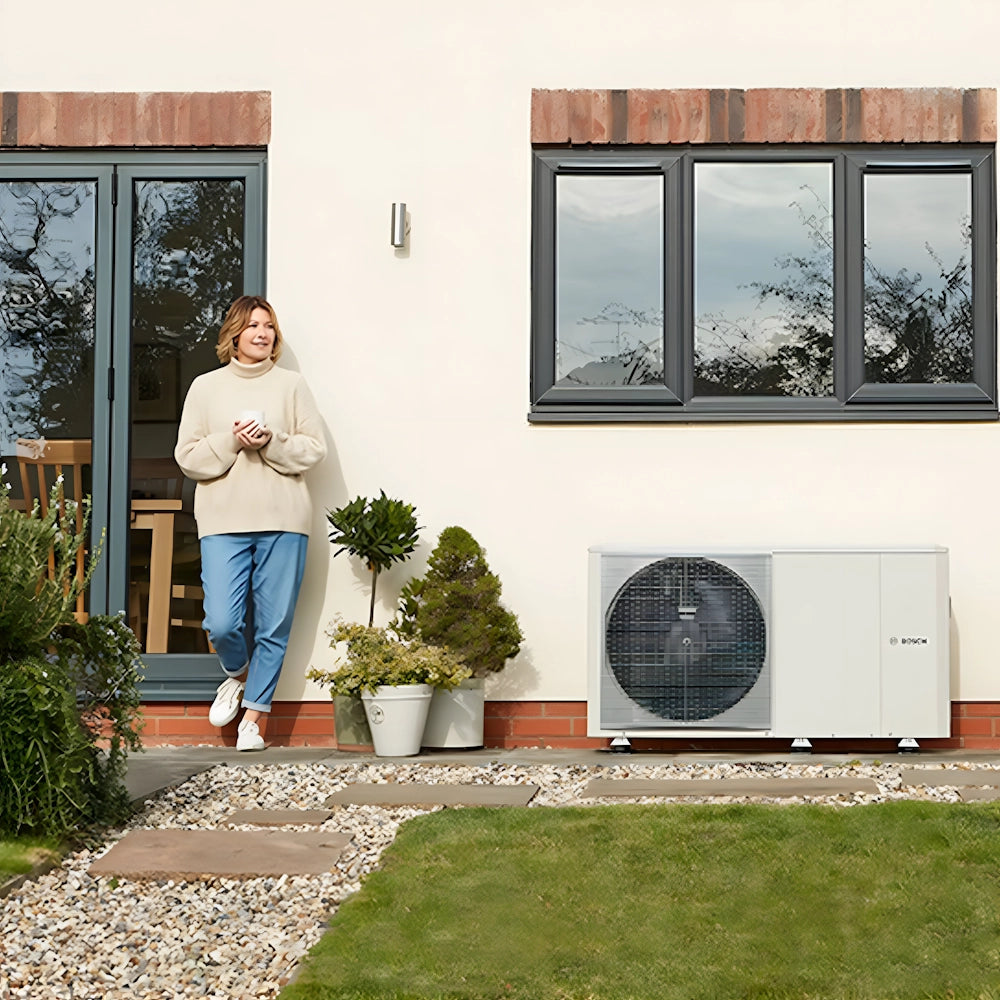 Woman standing beside Worcester Bosch Compress 2000 AWF heat pump at home, highlighting efficient heating solution.