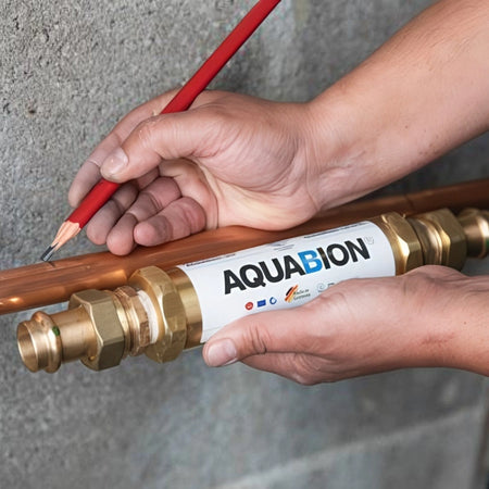 Person applying Aquabion water conditioner to a copper pipe with a red tool against a gray background